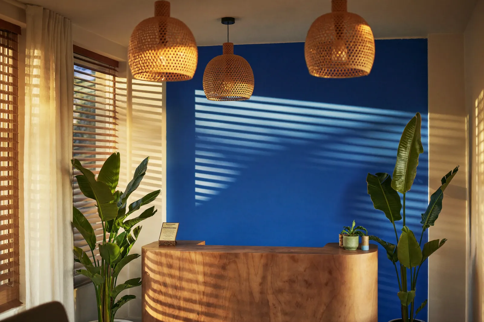 Villa Santé's warm reception with a natural wood desk, rattan pendant lights and a deep blue wall